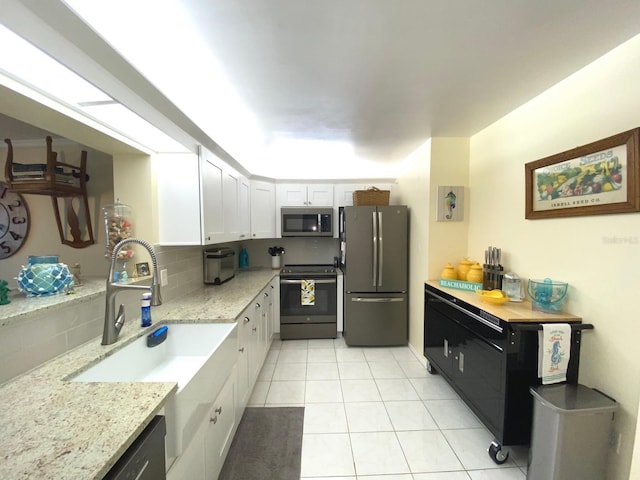 kitchen featuring decorative backsplash, appliances with stainless steel finishes, sink, light tile patterned floors, and white cabinetry