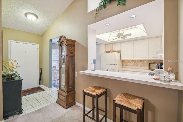 kitchen featuring white fridge, ceiling fan, a breakfast bar, light tile patterned floors, and backsplash