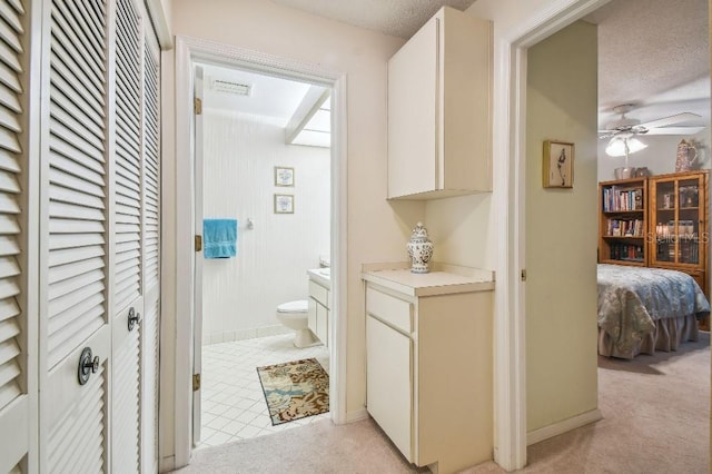 interior space with tile patterned flooring, a textured ceiling, toilet, vanity, and ceiling fan