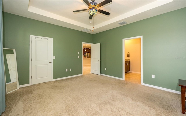 unfurnished bedroom with carpet flooring, a raised ceiling, ensuite bathroom, and ceiling fan