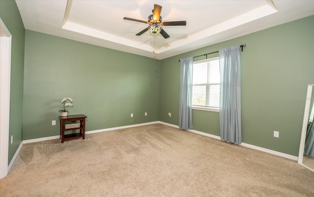 empty room with carpet flooring, ceiling fan, and a tray ceiling