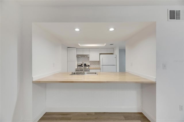 kitchen with sink, backsplash, kitchen peninsula, white fridge, and white cabinets