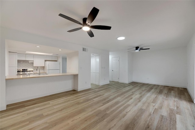 unfurnished living room with light wood-style flooring, a sink, visible vents, and baseboards