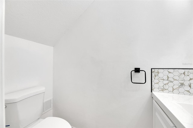 half bathroom with lofted ceiling, a textured ceiling, toilet, and vanity