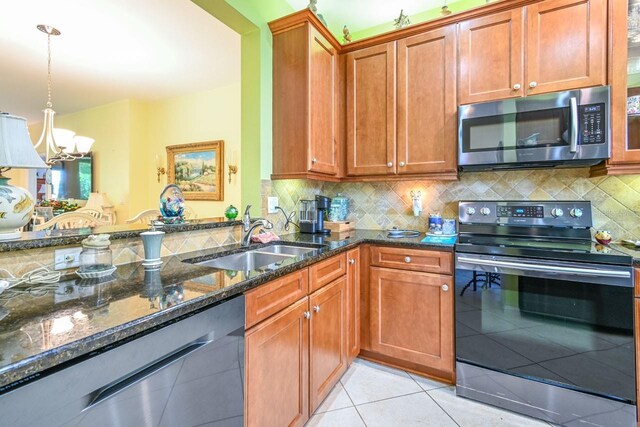 kitchen featuring stainless steel appliances, dark stone countertops, sink, backsplash, and light tile patterned flooring