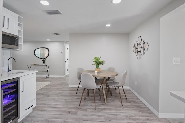 dining room featuring sink, light hardwood / wood-style flooring, and beverage cooler