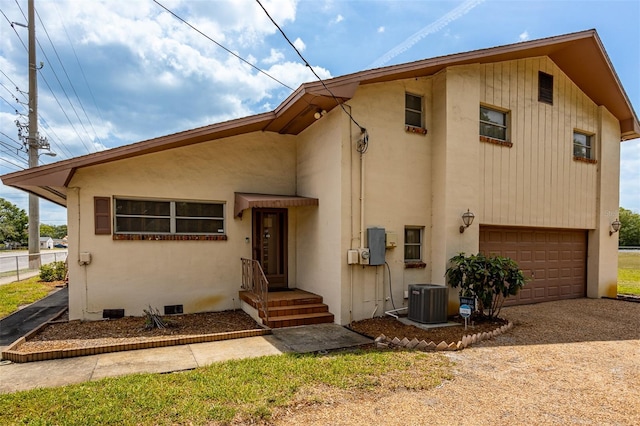 back of property featuring dirt driveway, stucco siding, central air condition unit, an attached garage, and crawl space