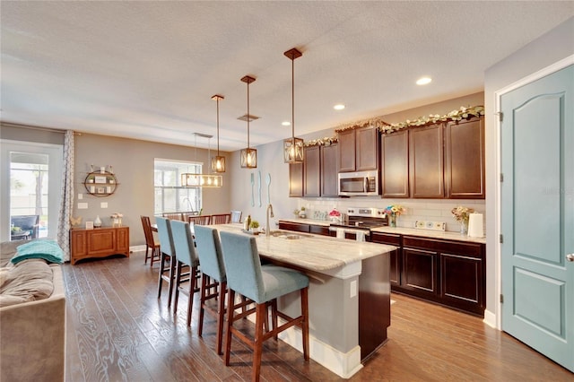 kitchen featuring a breakfast bar, a kitchen island with sink, hanging light fixtures, decorative backsplash, and stainless steel appliances