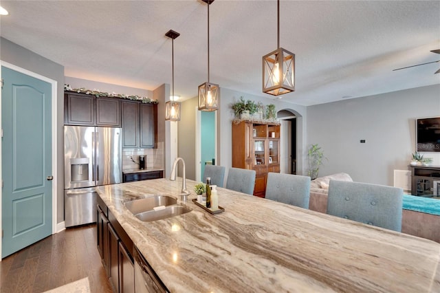 kitchen featuring dark brown cabinetry, sink, hanging light fixtures, dark hardwood / wood-style floors, and stainless steel fridge