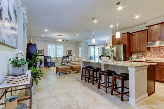 kitchen with a center island with sink, crown molding, ceiling fan, appliances with stainless steel finishes, and a kitchen bar