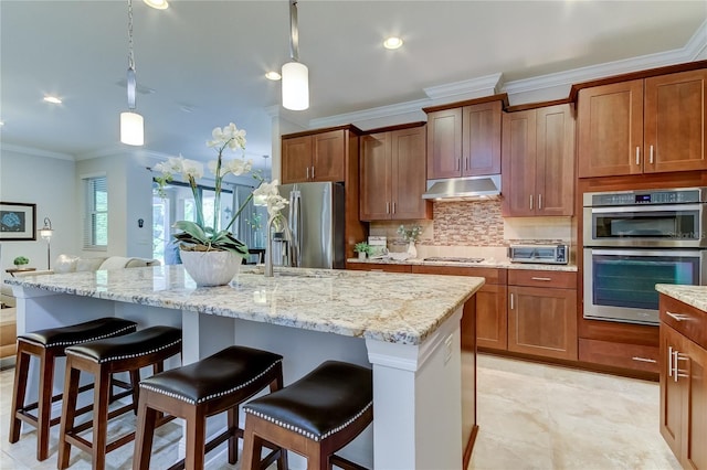 kitchen with stainless steel appliances, a kitchen breakfast bar, backsplash, pendant lighting, and a kitchen island with sink