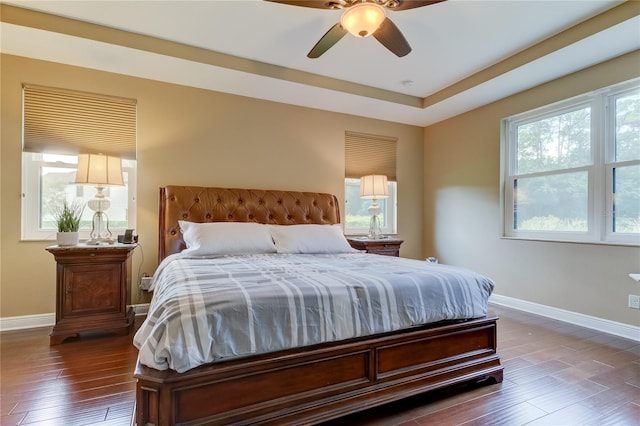 bedroom with a tray ceiling, ceiling fan, and dark wood-type flooring