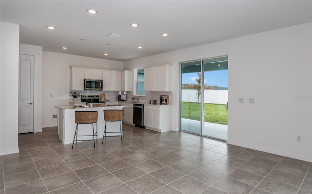 kitchen with a kitchen island, white cabinets, a kitchen breakfast bar, decorative backsplash, and stainless steel appliances