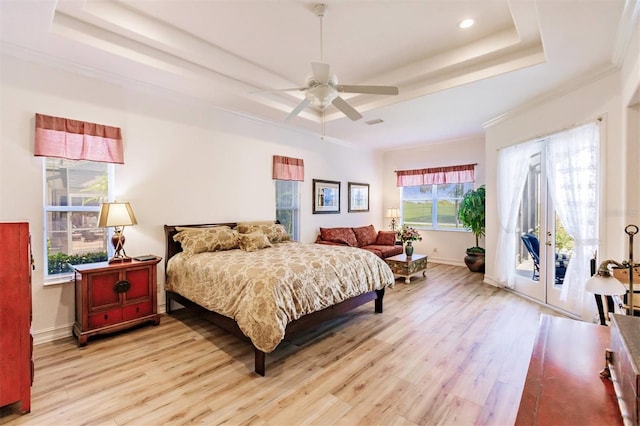 bedroom featuring light hardwood / wood-style flooring, a tray ceiling, multiple windows, and access to exterior