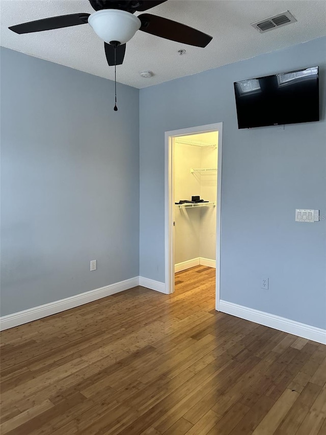 unfurnished bedroom with a textured ceiling, ceiling fan, dark hardwood / wood-style floors, and a walk in closet