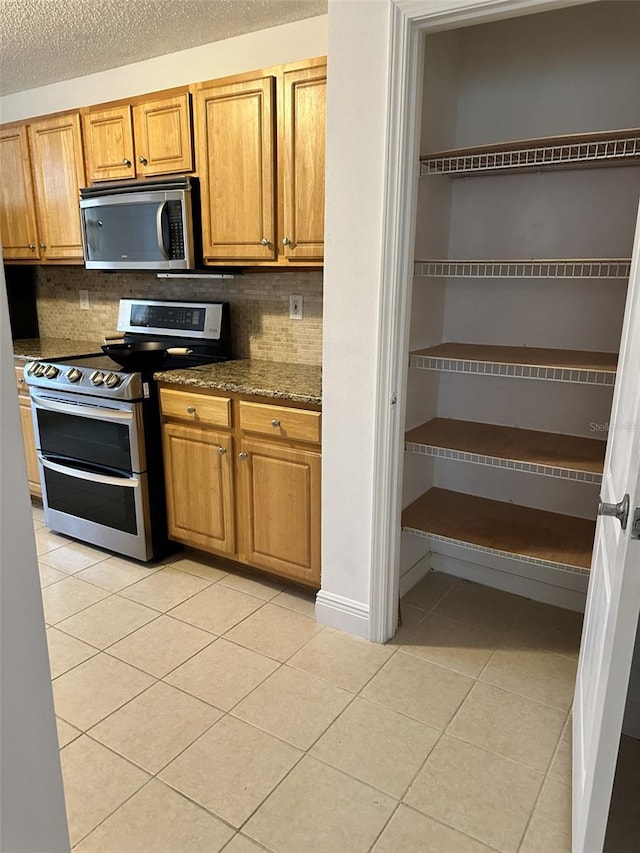 kitchen with tasteful backsplash, dark stone countertops, appliances with stainless steel finishes, a textured ceiling, and light tile patterned floors