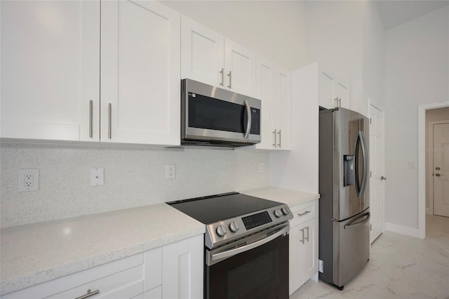 kitchen featuring stainless steel appliances, white cabinetry, light stone counters, and decorative backsplash