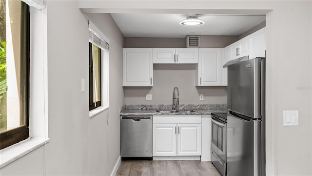 kitchen with sink, light hardwood / wood-style flooring, dark stone countertops, appliances with stainless steel finishes, and white cabinets