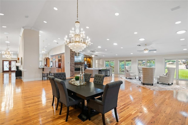 dining room with ceiling fan with notable chandelier, ornamental molding, light hardwood / wood-style flooring, and a brick fireplace