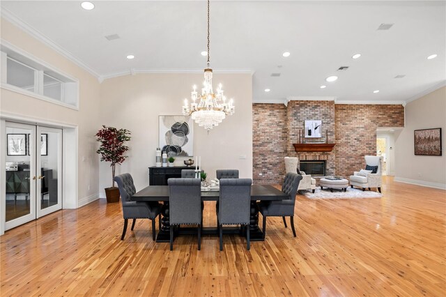 dining space with a fireplace, an inviting chandelier, light hardwood / wood-style flooring, and ornamental molding