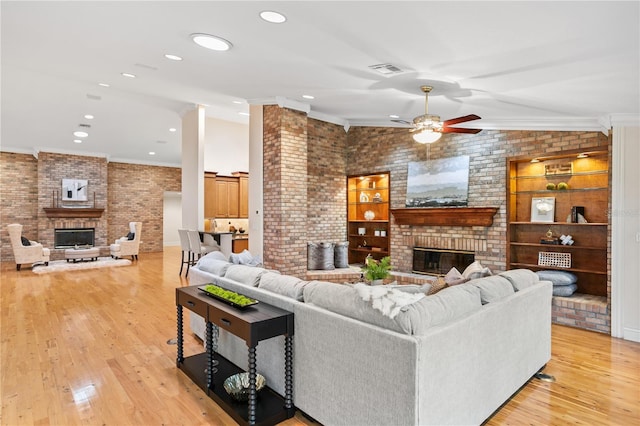 living room with vaulted ceiling, ceiling fan, light wood-type flooring, ornamental molding, and a fireplace