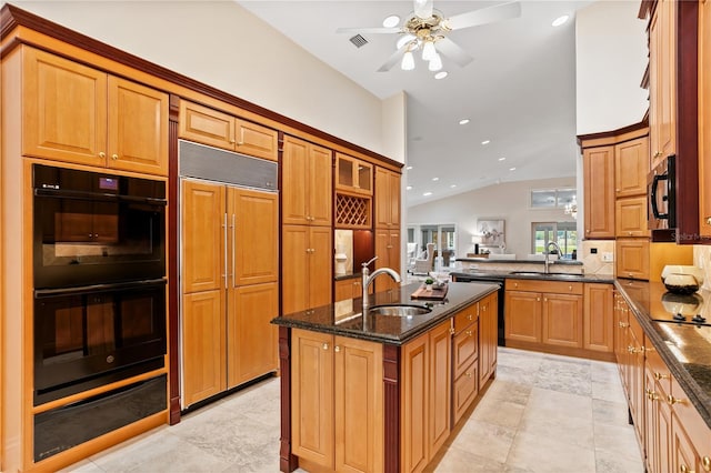 kitchen featuring sink, a kitchen island with sink, dark stone countertops, and black appliances