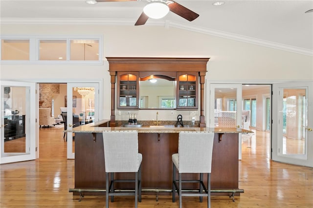 kitchen with ornamental molding, ceiling fan, light hardwood / wood-style flooring, a breakfast bar area, and lofted ceiling