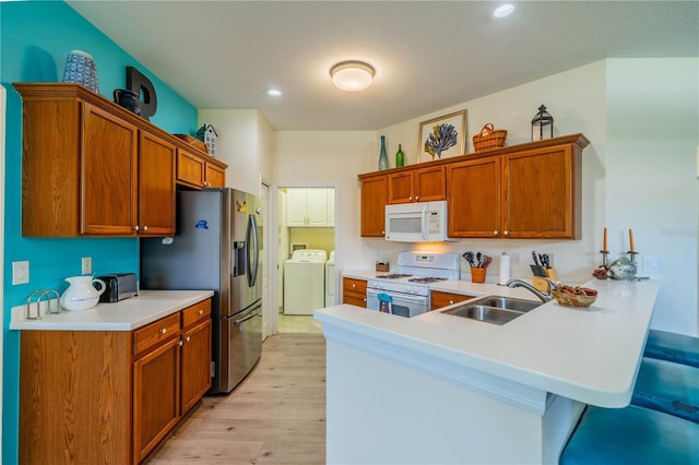 kitchen with washing machine and clothes dryer, sink, a breakfast bar area, kitchen peninsula, and white appliances