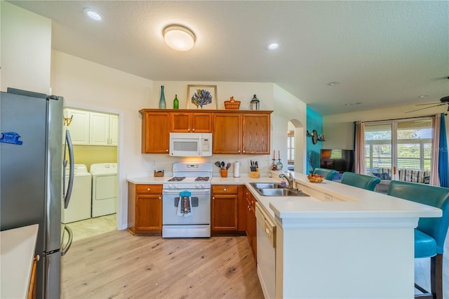 kitchen featuring sink, a breakfast bar area, kitchen peninsula, washing machine and dryer, and white appliances