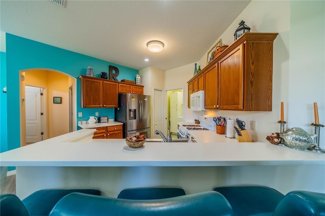 kitchen featuring white appliances, a kitchen bar, kitchen peninsula, and sink