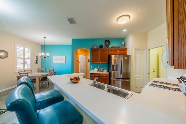 kitchen with sink, light hardwood / wood-style flooring, a kitchen bar, stainless steel fridge with ice dispenser, and decorative light fixtures