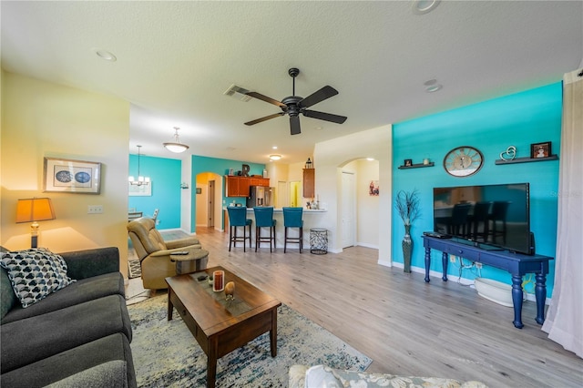 living room featuring ceiling fan with notable chandelier, a textured ceiling, and light hardwood / wood-style flooring