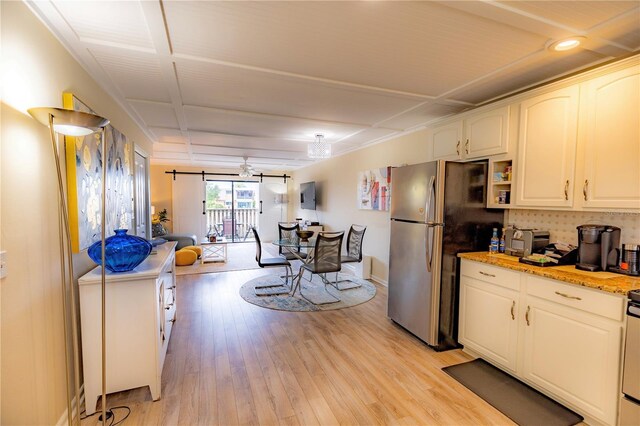 kitchen with light stone countertops, stainless steel fridge, light wood-type flooring, ceiling fan, and white cabinetry