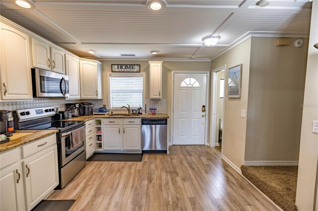 kitchen featuring sink, appliances with stainless steel finishes, tasteful backsplash, light hardwood / wood-style floors, and light stone counters