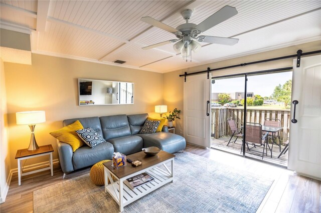 living room with hardwood / wood-style flooring, ceiling fan, a barn door, and crown molding