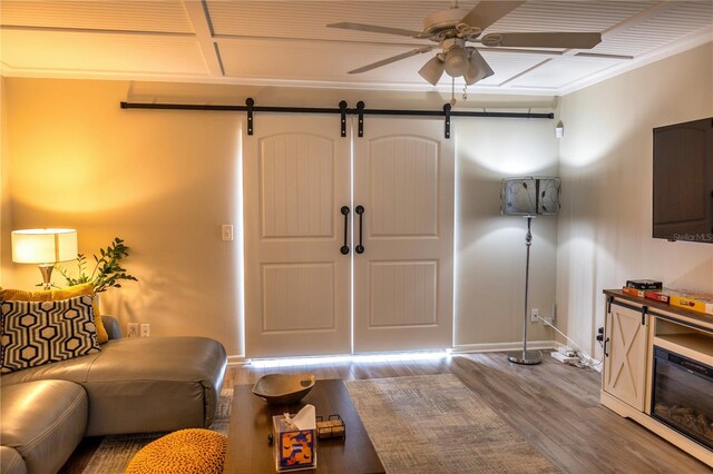 foyer with a barn door, ceiling fan, crown molding, and wood-type flooring