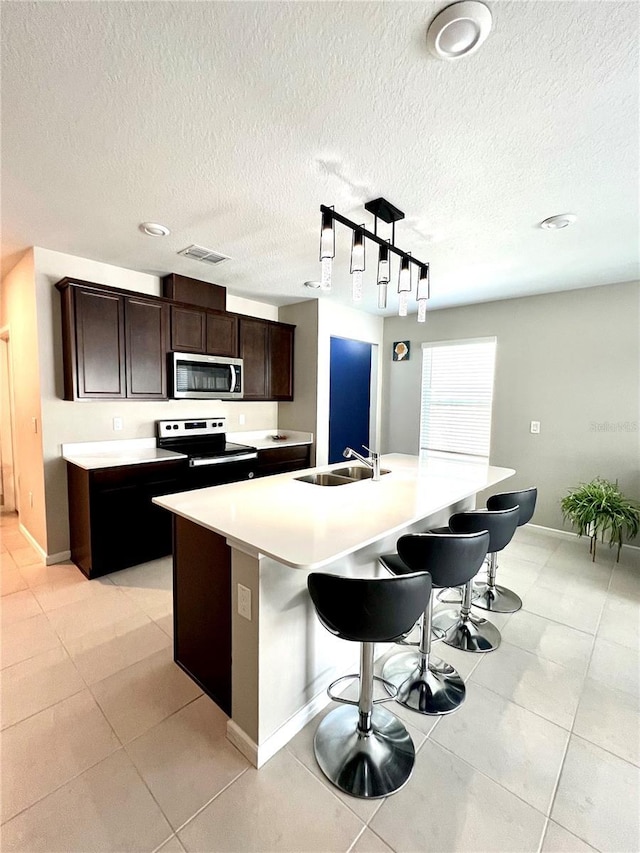 kitchen with dark brown cabinetry, sink, stainless steel appliances, and an island with sink