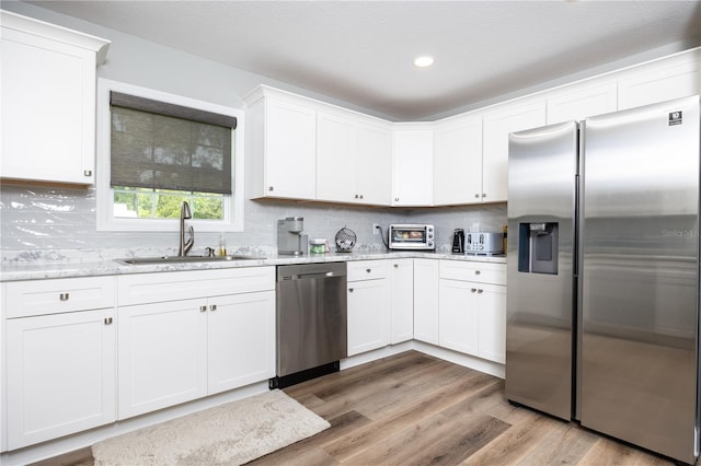 kitchen featuring stainless steel appliances, white cabinetry, light stone countertops, and sink