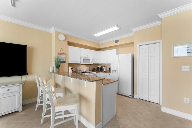 kitchen with kitchen peninsula, dark stone counters, white appliances, light tile patterned floors, and white cabinetry