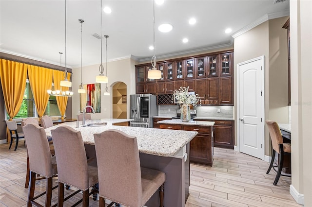 kitchen with sink, hanging light fixtures, a kitchen breakfast bar, stainless steel fridge, and an island with sink