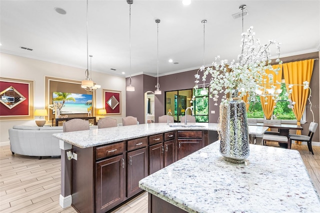 kitchen with light stone countertops, hanging light fixtures, a large island, and sink