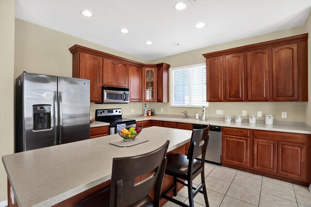 kitchen with light tile patterned floors, appliances with stainless steel finishes, a center island, a kitchen breakfast bar, and sink