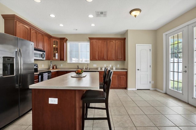 kitchen featuring a kitchen island, plenty of natural light, stainless steel appliances, light tile patterned floors, and french doors