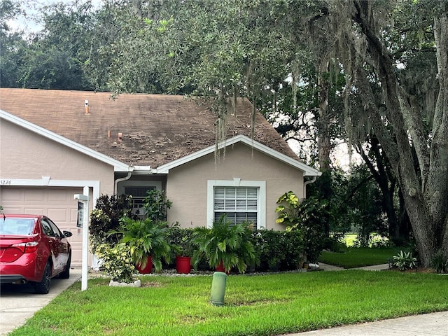 single story home featuring a garage, a front yard, and stucco siding