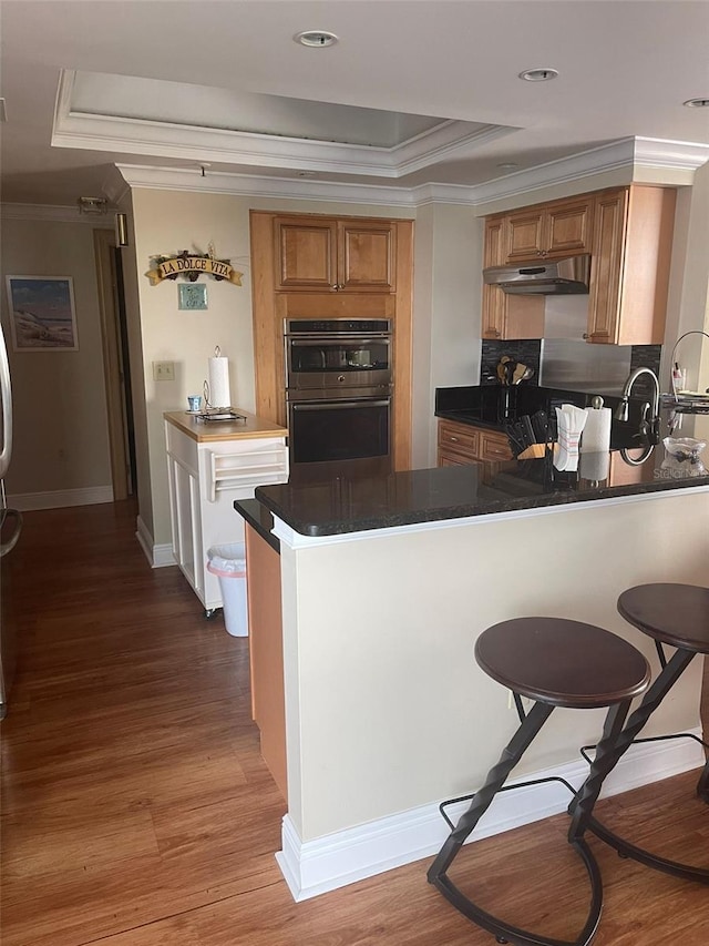 kitchen featuring kitchen peninsula, light hardwood / wood-style floors, stainless steel double oven, and a raised ceiling