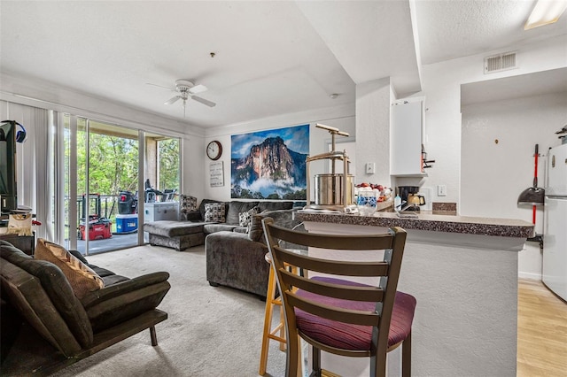 living room with ceiling fan, a textured ceiling, and light hardwood / wood-style floors