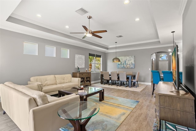 living room featuring light wood-type flooring, a tray ceiling, ceiling fan, and crown molding