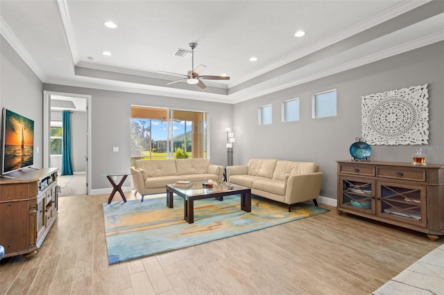 living room with a raised ceiling, light wood-type flooring, and ornamental molding