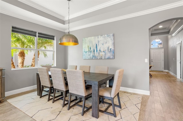 dining space with a tray ceiling, ornamental molding, and light wood-type flooring