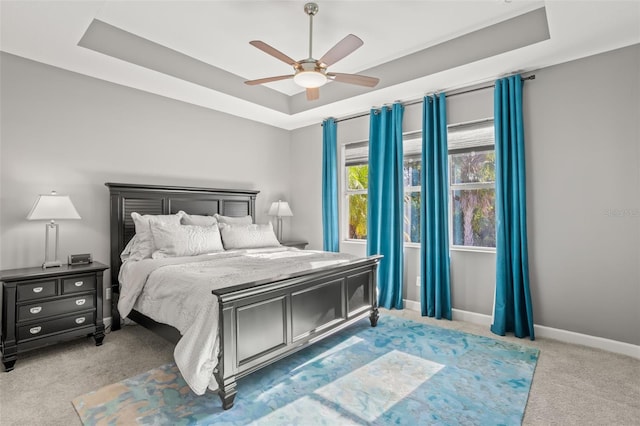 carpeted bedroom featuring a raised ceiling and ceiling fan